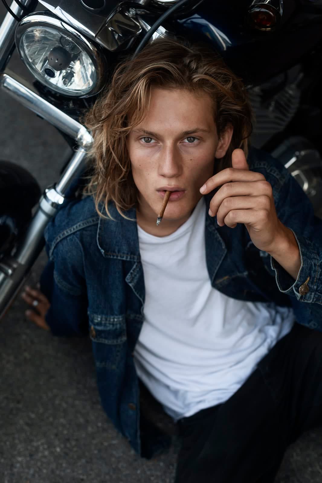 Model lying on the asphalt beside a motorcycle, shot from above