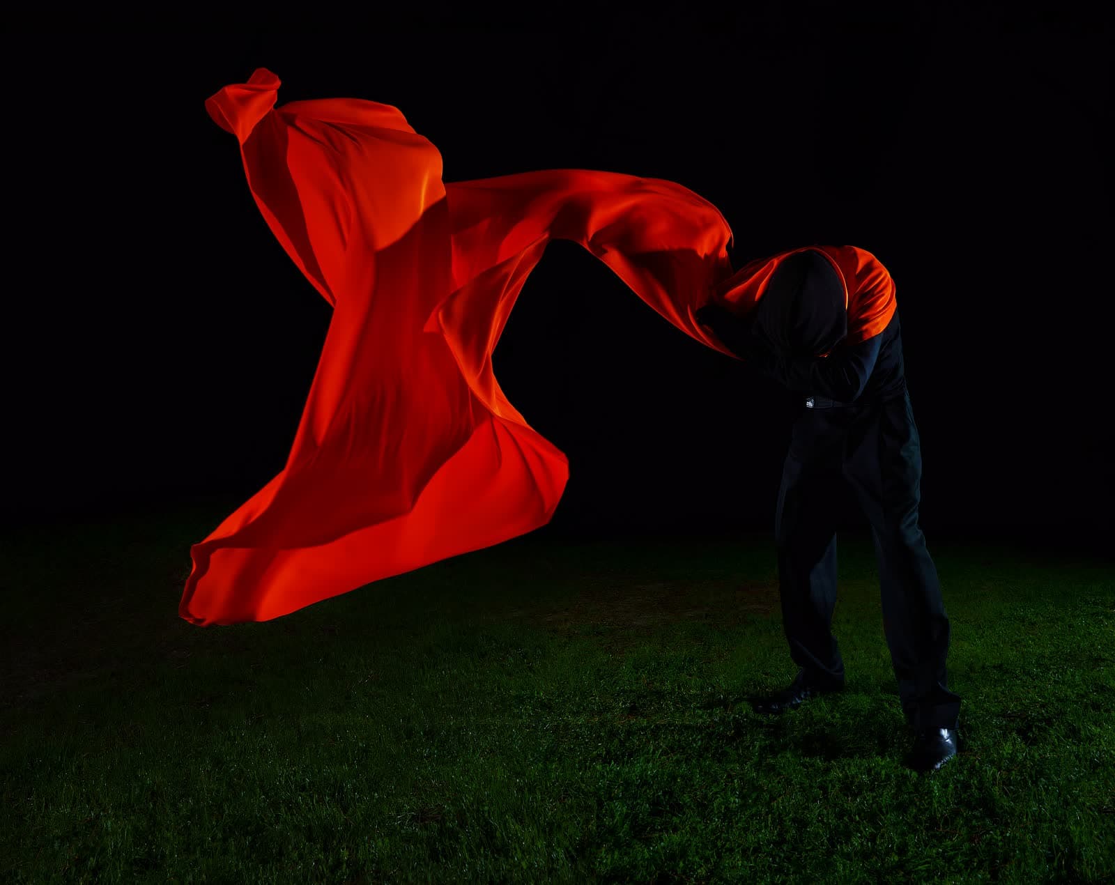 Une étoffe rouge en vol au-dessus de l'herbe nocturne, une silhouette en noir derrière