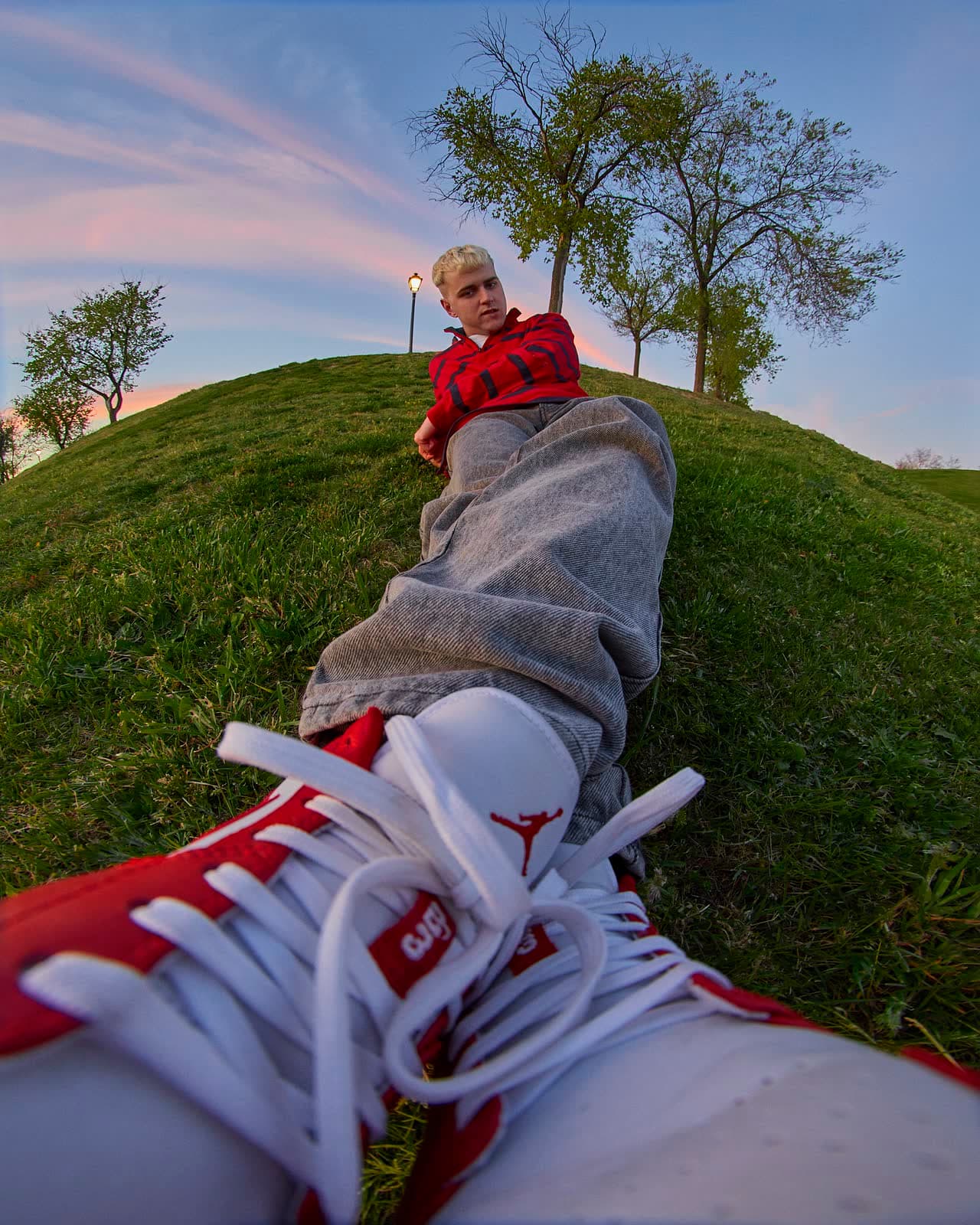 Point-of-view frame: red high-tops and a figure on a green hill under a wide sky