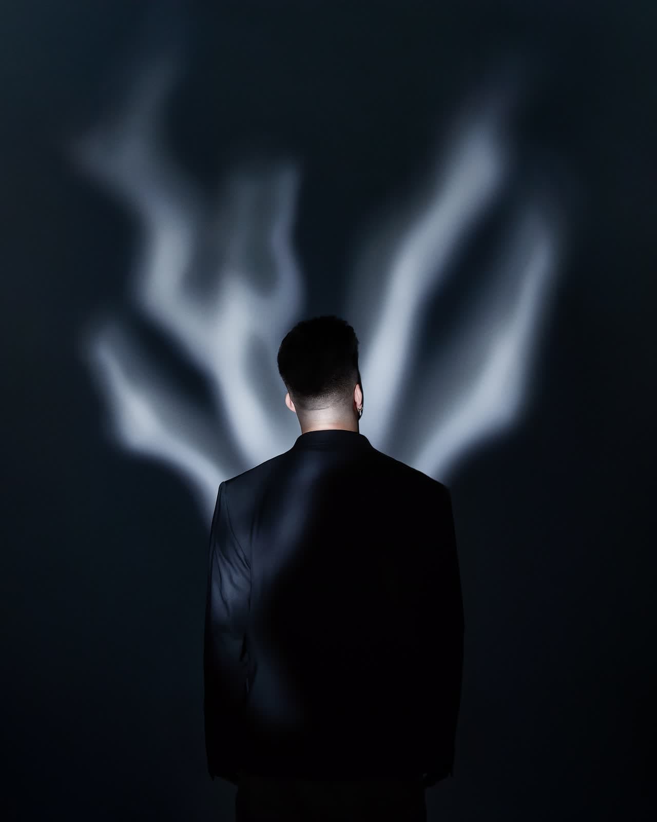 Figure in a black suit from behind, smoke rising like wings