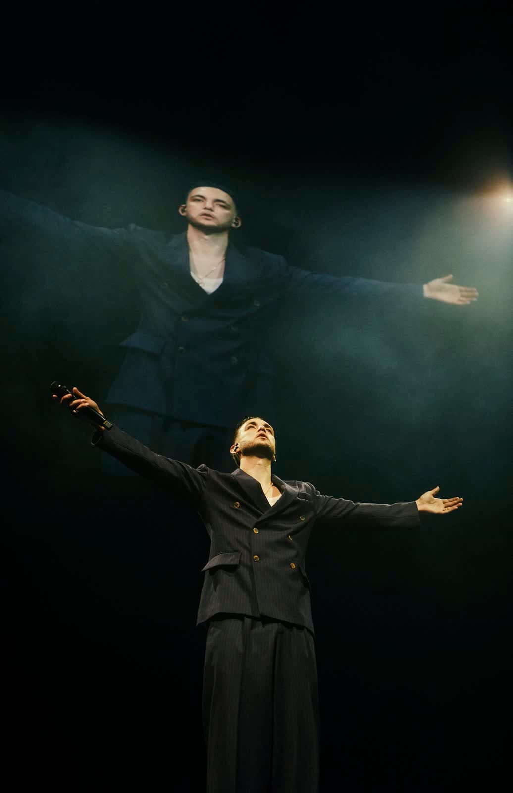 Singer with arms open in a beam of light on stage
