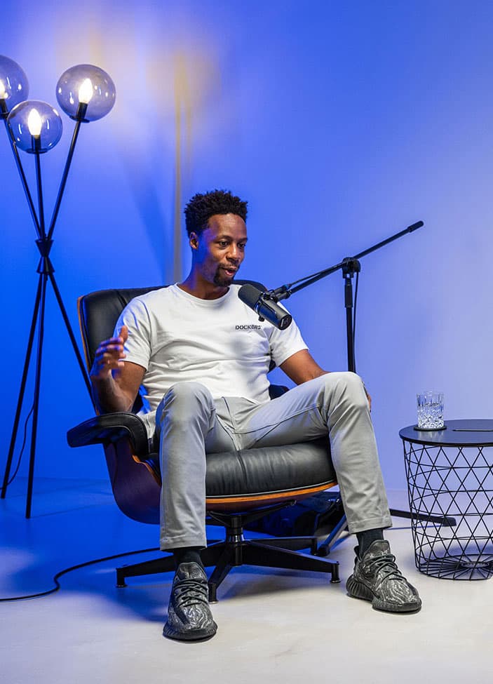 Gaël Monfils gesticulant en parlant au micro sur le plateau de podcast éclairé en bleu