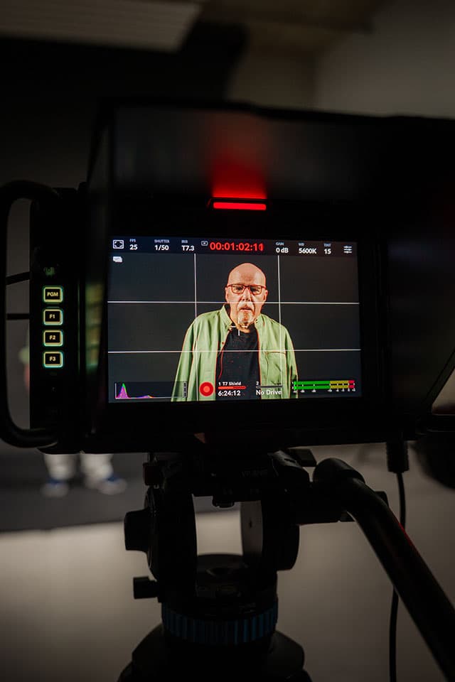 Close-up of a camera monitor showing Paolo Coelho in a green shirt during a video recording