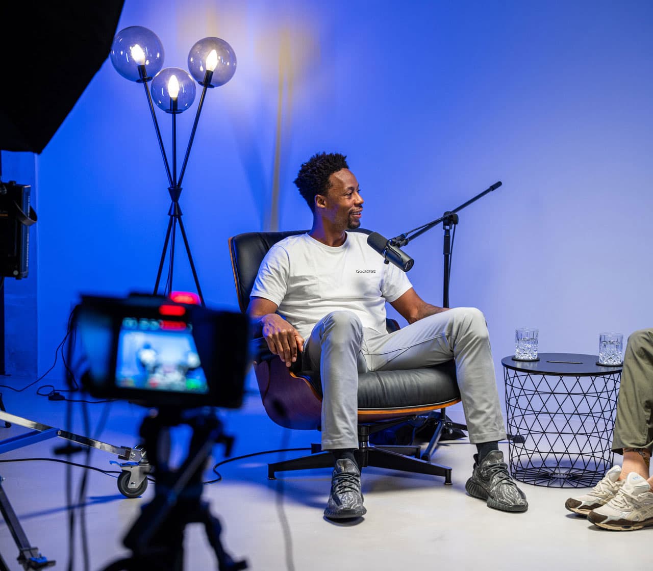Gaël Monfils parlant au micro dans un fauteuil en cuir, une caméra de tournage au premier plan