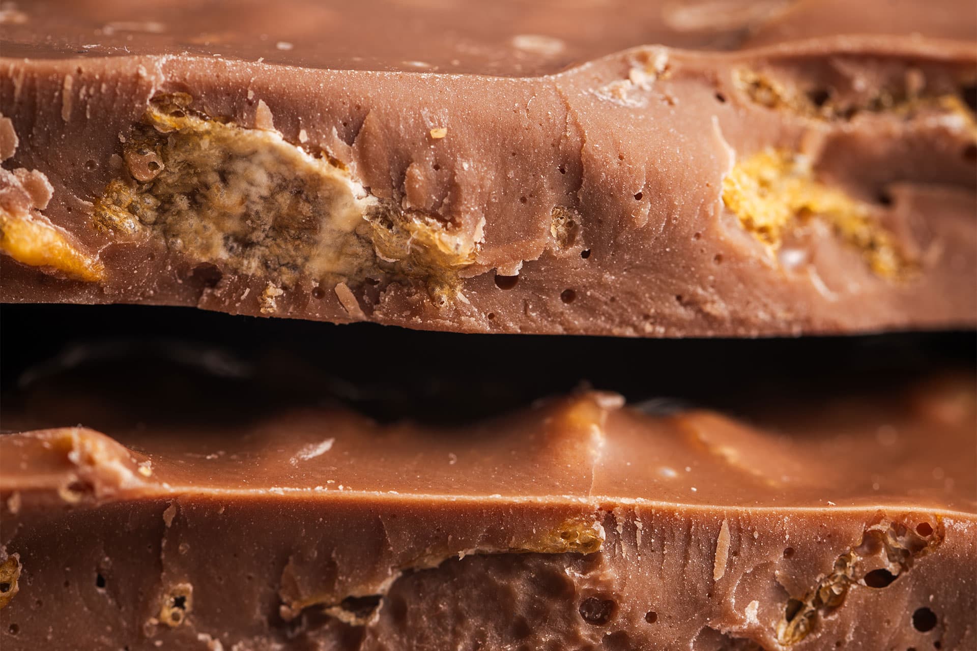 Macro close-up of stacked broken milk chocolate pieces with crunchy caramel inclusions