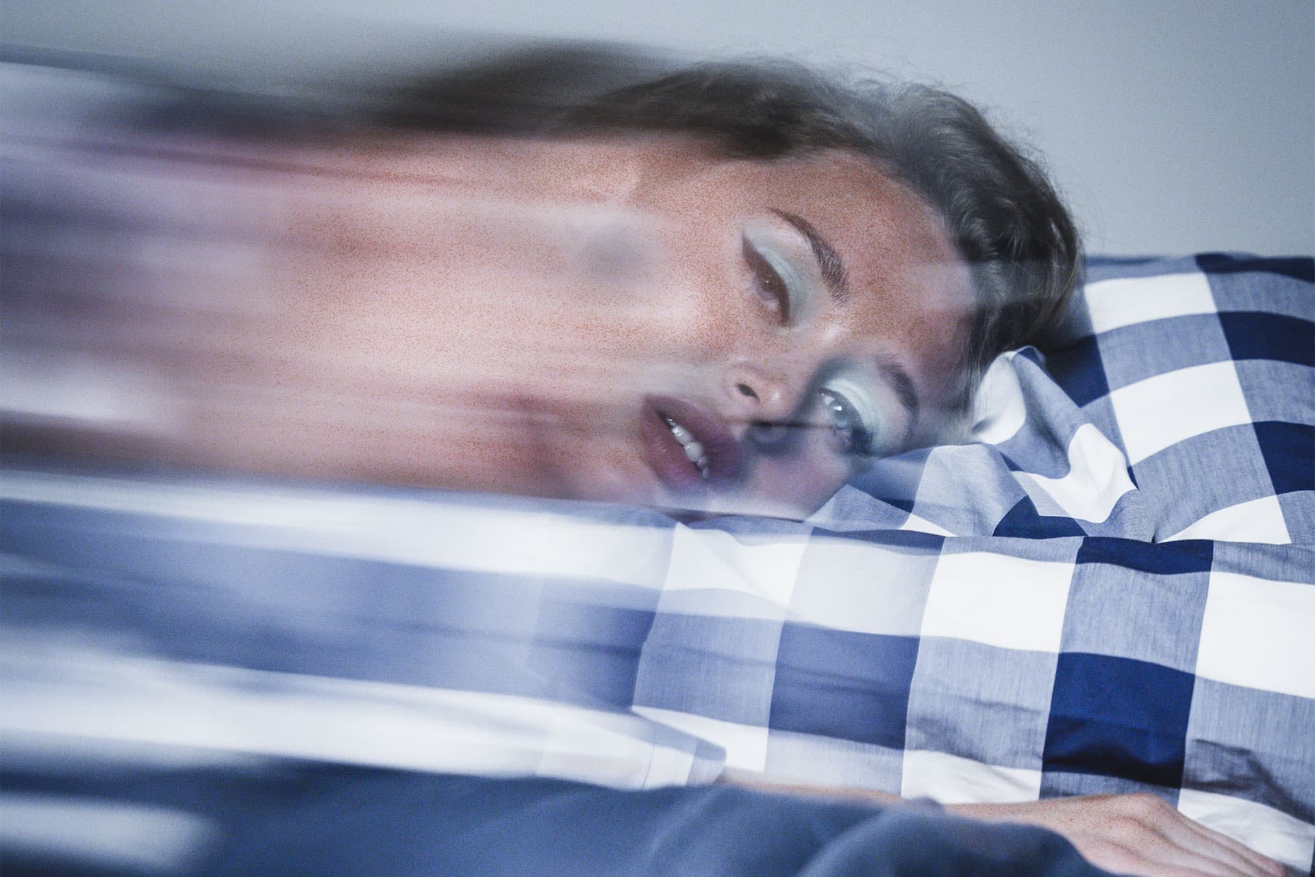 Femme allongée sur un oreiller vichy bleu et blanc, les yeux mi-clos, filé de mouvement traversant l'image