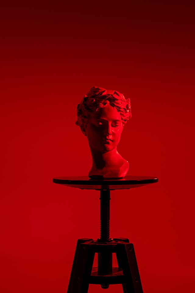 Classical plaster head with laurel wreath on a black stool, bathed in monochrome red light