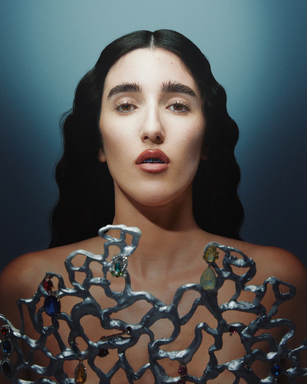 Beauty portrait with a liquid-metal neckpiece on a blue backdrop