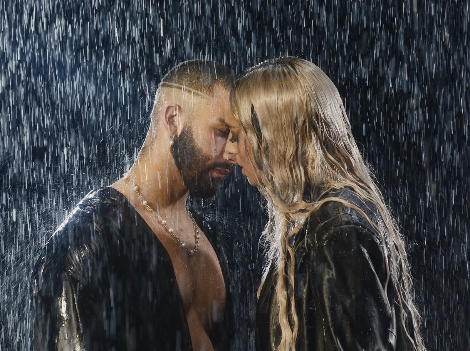 Two people face to face under heavy rain, lit from behind